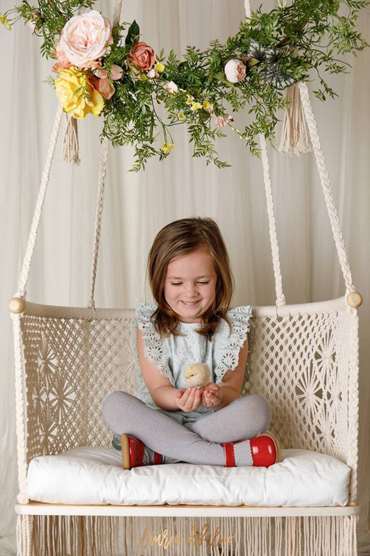 kid girl sitting on a swing chair watching a chick in her hands