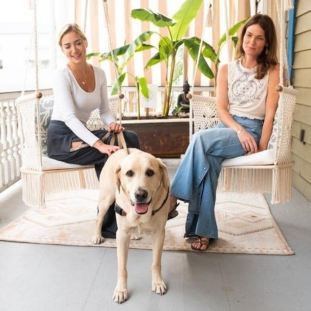 one woman sitting on a swing chair while keeping a dog on a leash, another woman sitting on another swing chair looking the dog