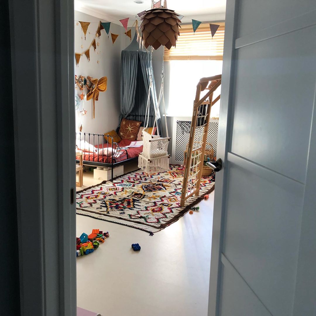 baby swing chair hanging in a play room with colorful carpet and a metal bed