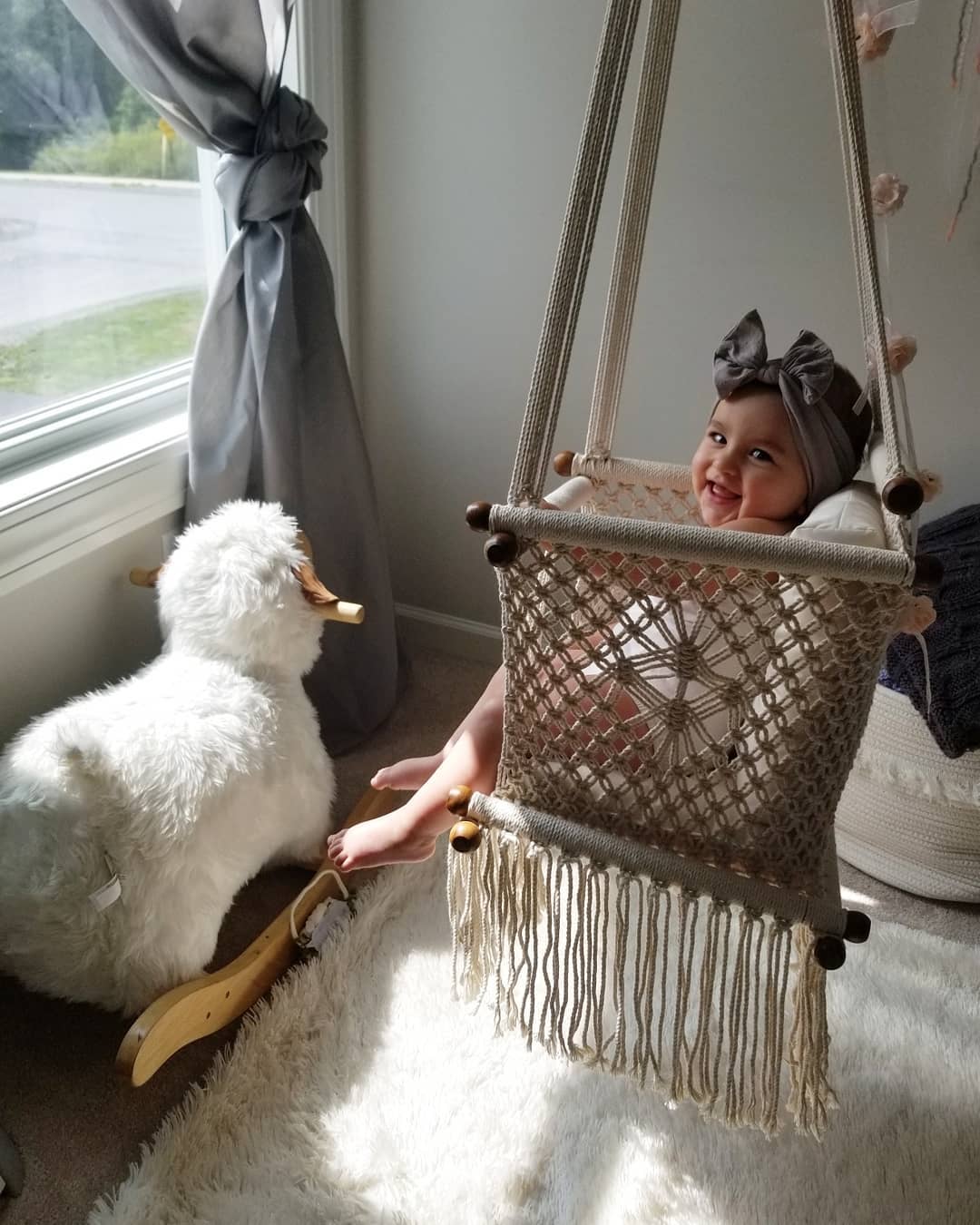 baby smiling while is swinging on a swing chair in front of a window 