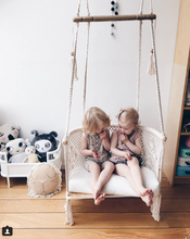 two kids talking and eating sweets while they are sitting on a hanging chair